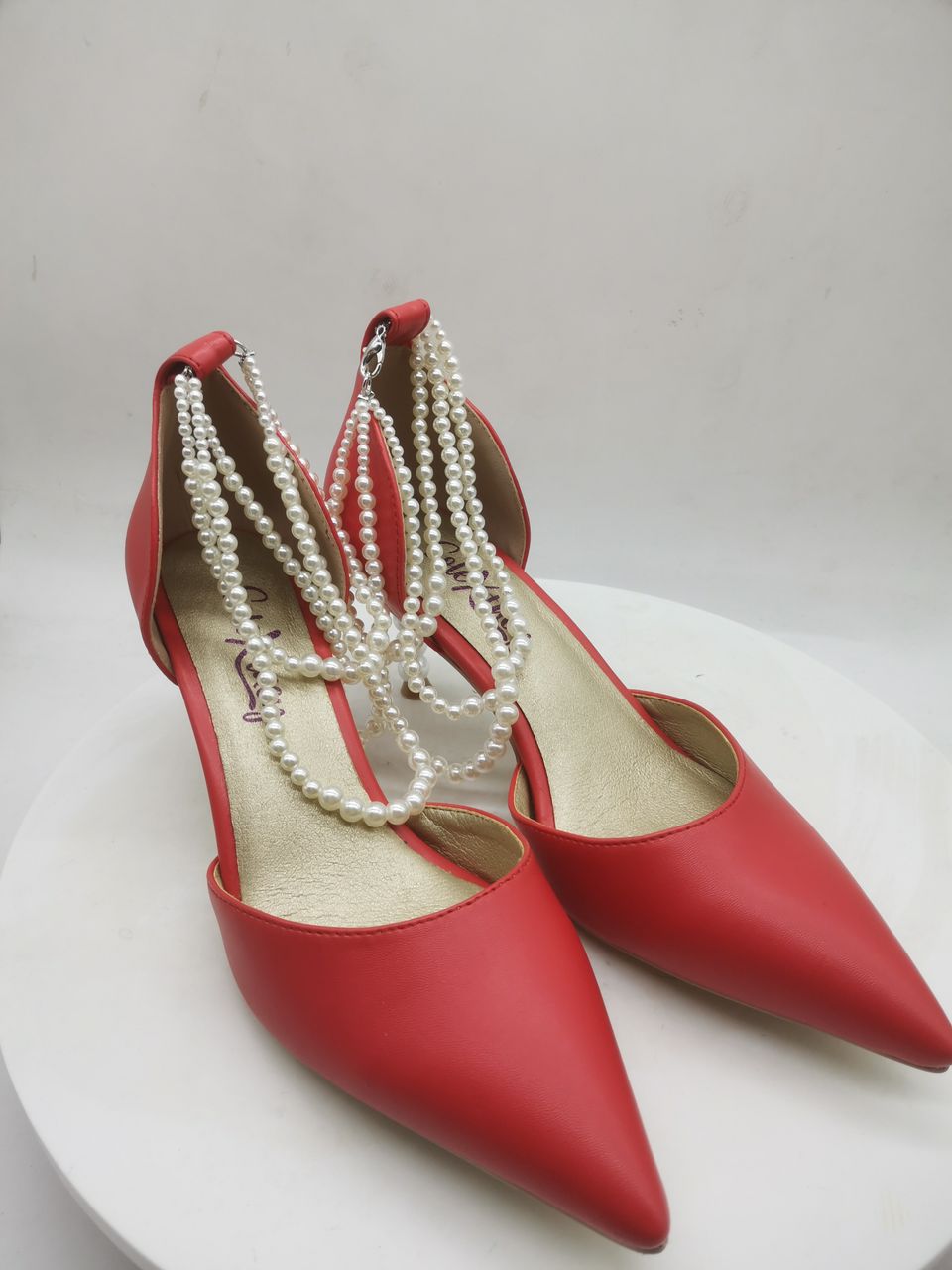 Red pointed heeled pumps with white pearl-bead ankle straps and metal heel