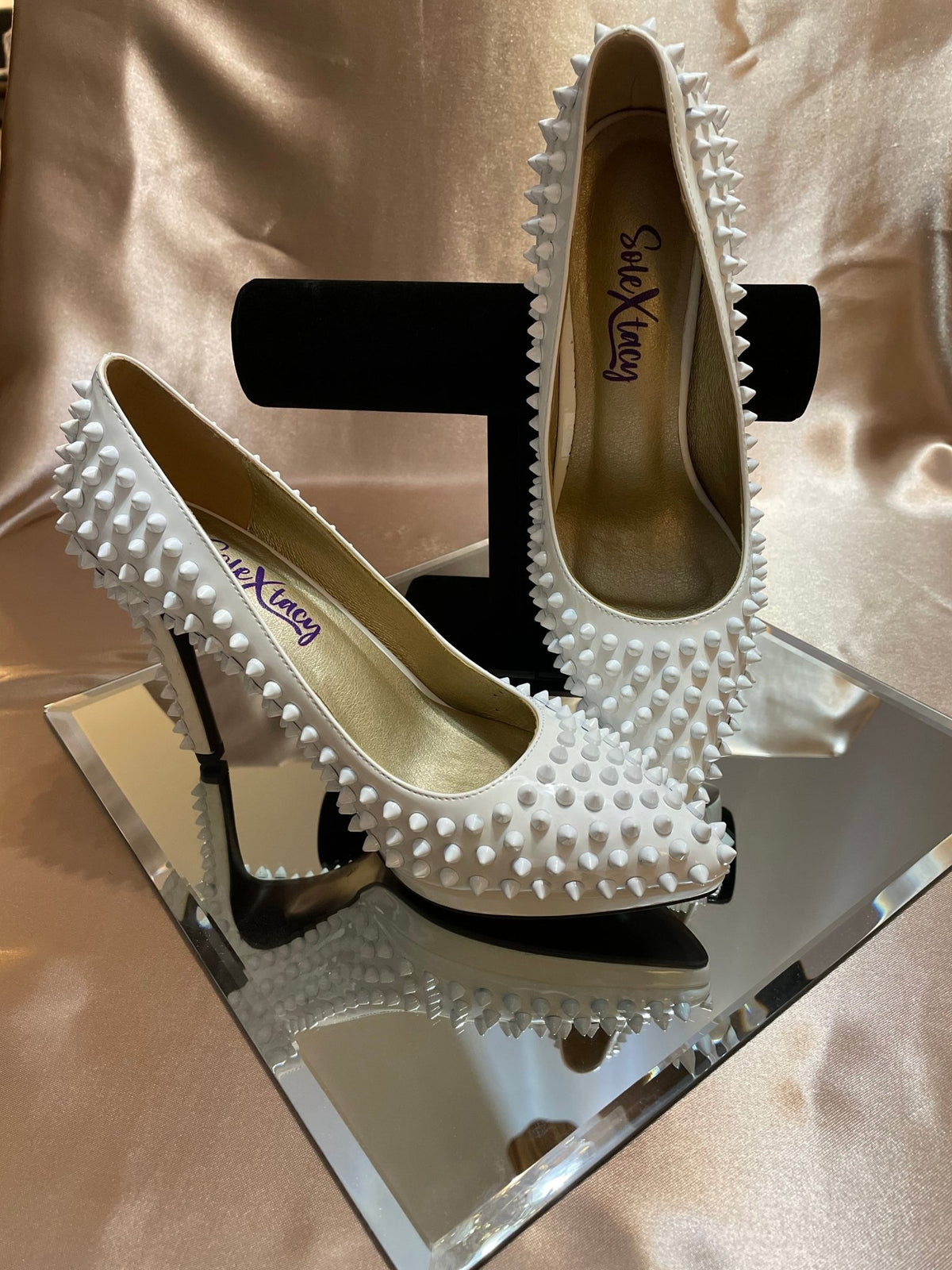 Pair of white spike-studded pointed-toe shoes with black heel, backs and sides visible.