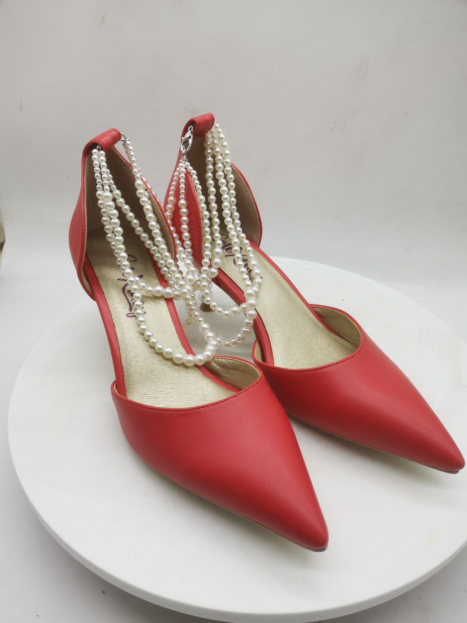 Red pointed heeled pumps with long white pearl-bead ankle straps