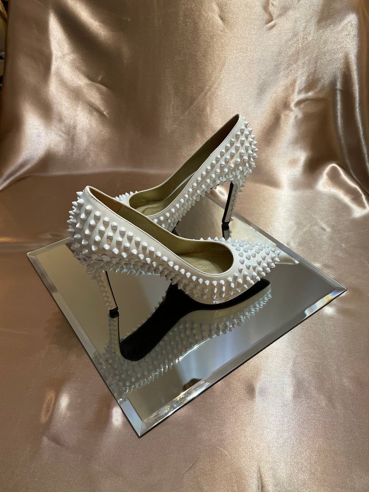 White spike-studded pointed-toe shoe, side view, black sole detail.