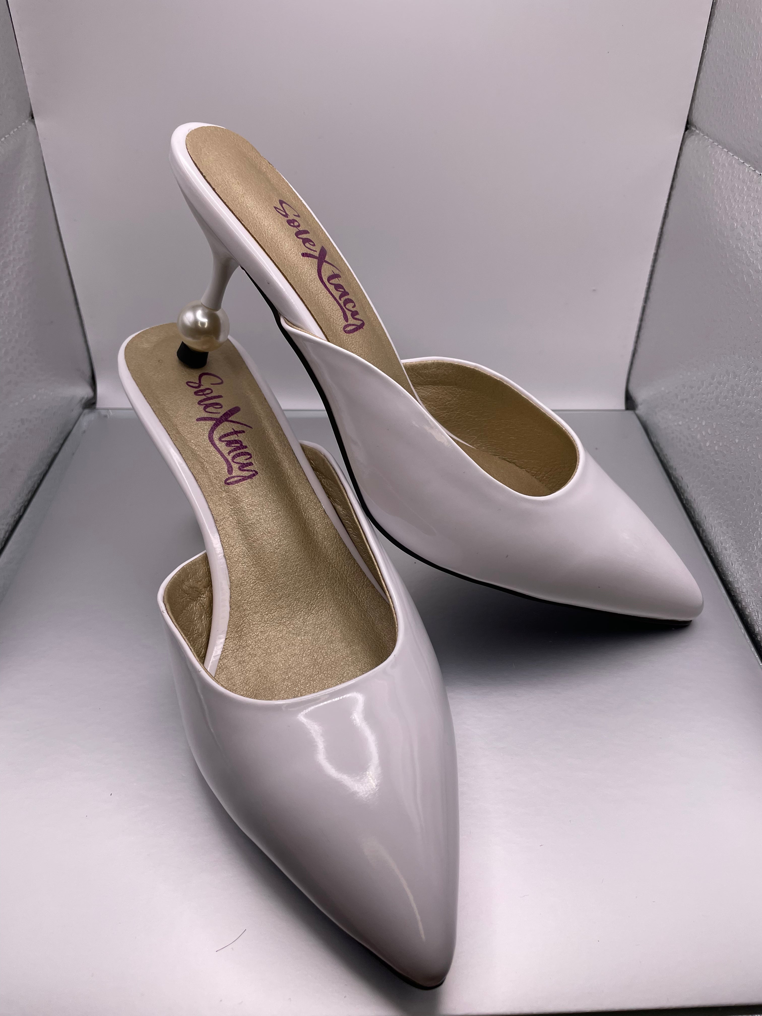 White pointed-toe mule heels, glossy finish, gold-toned heel caps